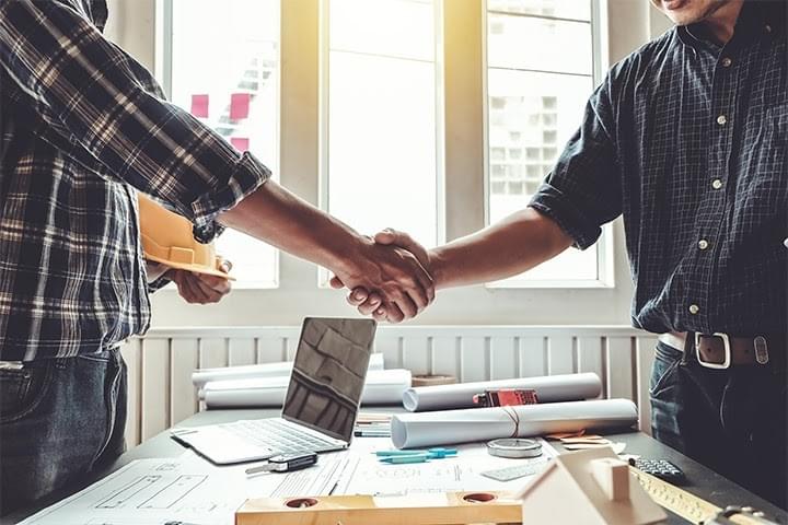 contractor and architect shake hands over completed home remodel blueprint